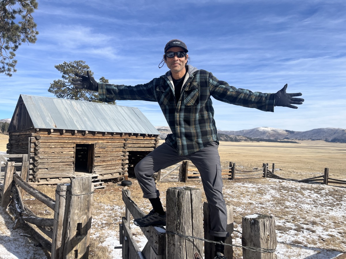 Standing outdoors with arms wide on a log fence.